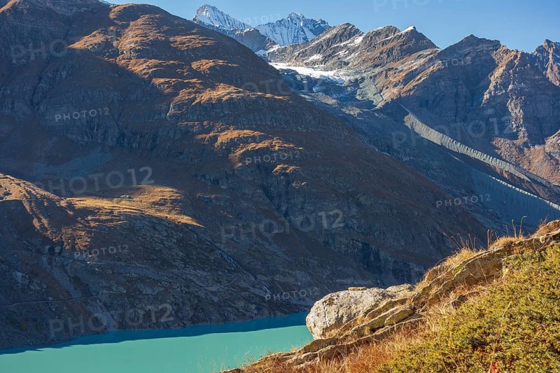 A mountain lake under bright sunlight, surrounded by autumn-coloured mountains and snow-capped peaks, Saas Fee, Switzerland, Europe