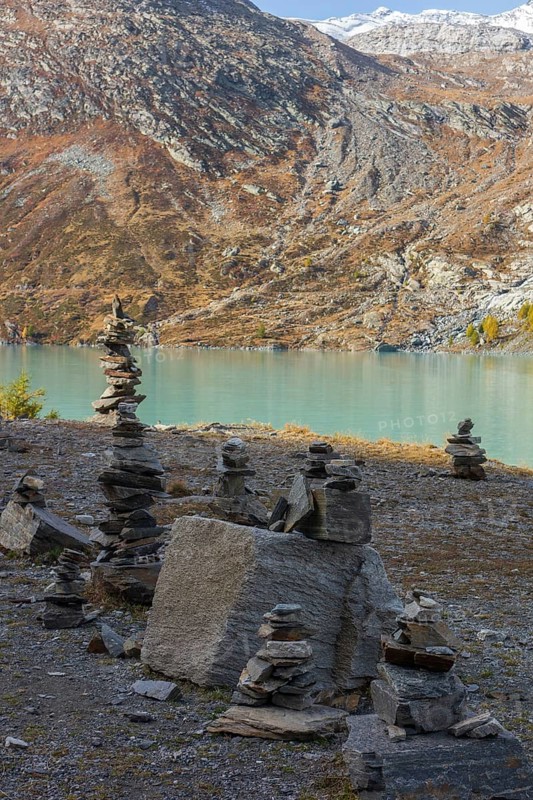 Piles of stones balancing artfully on the shore of a lake in a tranquil mountain landscape, Saas Fee, Switzerland, Europe