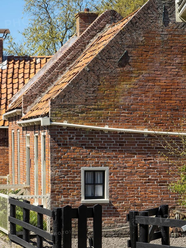 A rustic brick building with a wooden fence and bricks, in a rural setting, enkhuizen, the netherlands