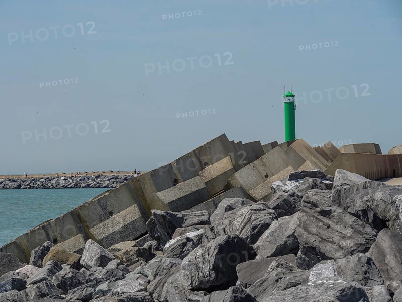 Stable rock formations and a green lighthouse at the breakwater along the coast under a clear sky, oostende, Belgium, Europe