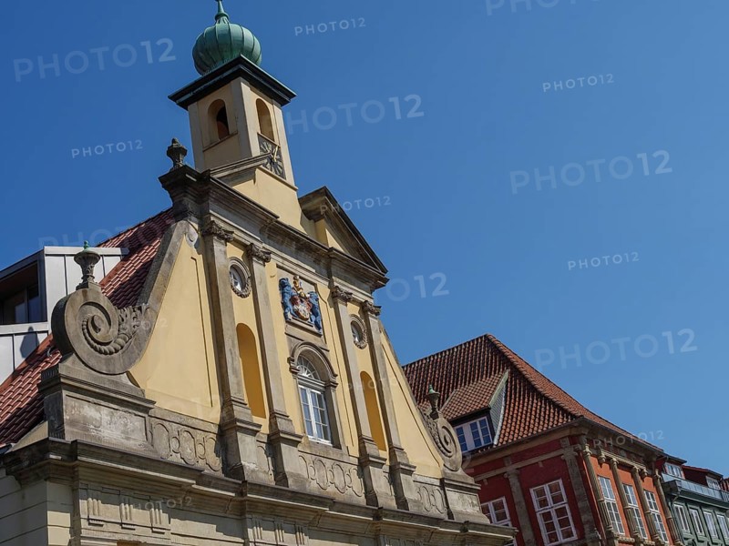 Baroque building in the old town centre with a pale church tower in the background under a blue sky, lüneburg, germany