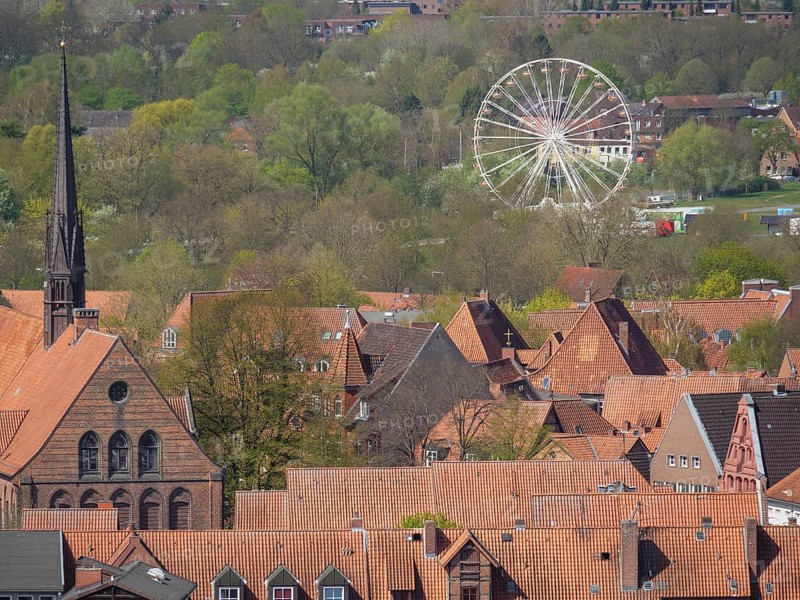 Cityscape with church tower, red roofs, green foliage and a holiday bike in the background under a blue sky, lüneburg, germany