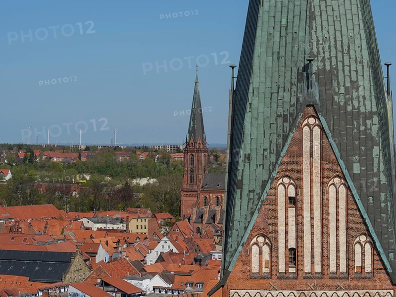 Church towers and roofs of a town, surrounded by landscape and wind turbines in the background, lüneburg, germany