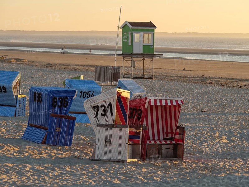 Several colourful beach chairs are scattered on the beach at sunset, with a green guardhouse, langeoog, germany