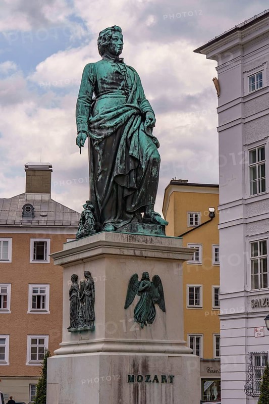 Monument to Mozart on a square surrounded by historic buildings under a cloudy sky, Salzburg, Austria, Europe