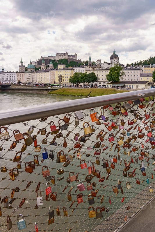 Love locks on a bridge railing with a view of historic buildings along a river, Salzburg, Austria, Europe
