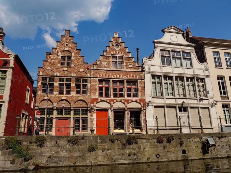 A row of old brick and faÃ§ade buildings along a canal in sunny weather, gent, belgium
