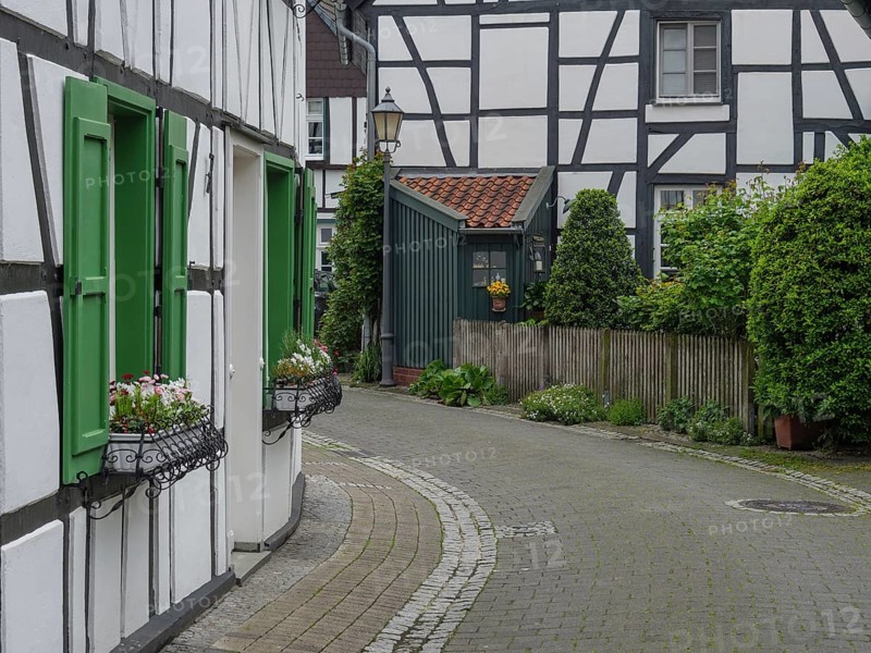 Narrow cobbled street with half-timbered houses and green shutters in a German village, Westerholt, Herten Ruhr area, North Rhine-Westphalia, Germany, Europe