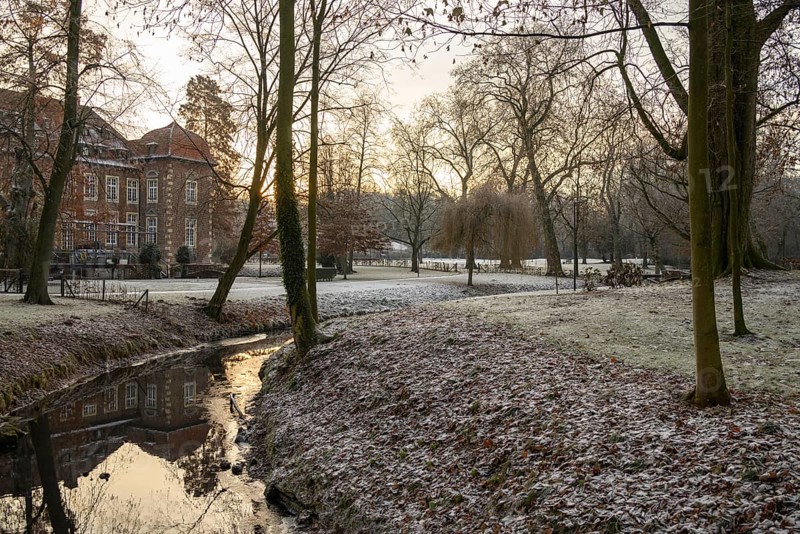 A small stream with a reflection flows through a frosty park, in the background a large building and bare trees, Velen, North Rhine-Westphalia, GERMANY