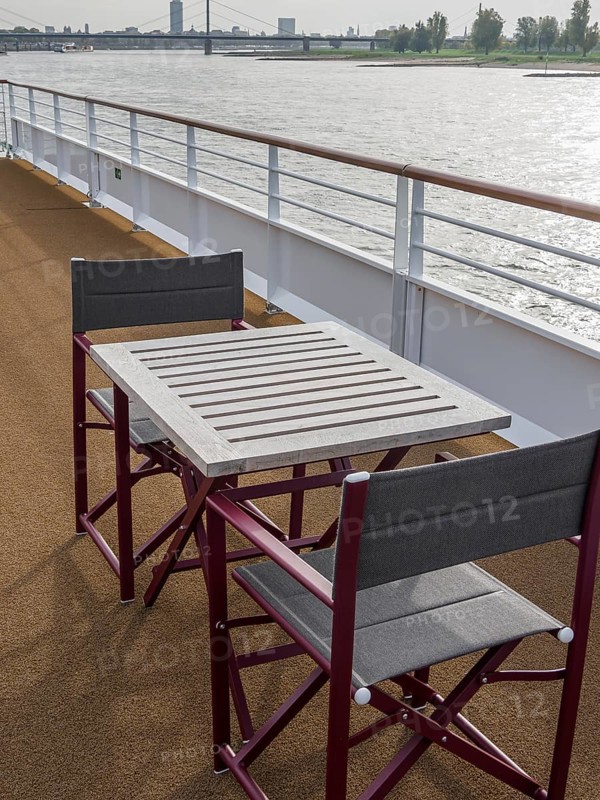 Deck of a ship with table and chairs, view of the river and the surrounding landscape. The railing and the sky are clearly visible, Düsseldorf, North Rhine-Westphalia, GERMANY