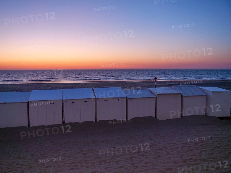 White beach huts at dusk, with an intensely coloured sunset and calm sea, de haan, Belgium, Europe