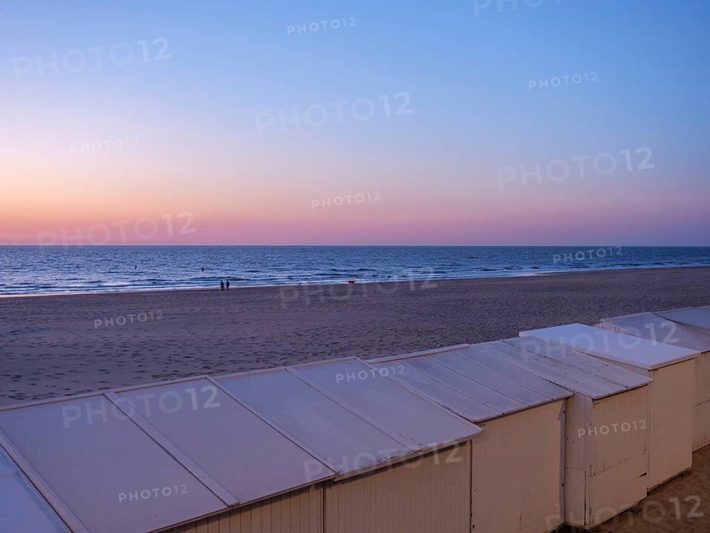 White huts stand on a quiet beach as the sun sets under a purple sky, de haan, Belgium, Europe