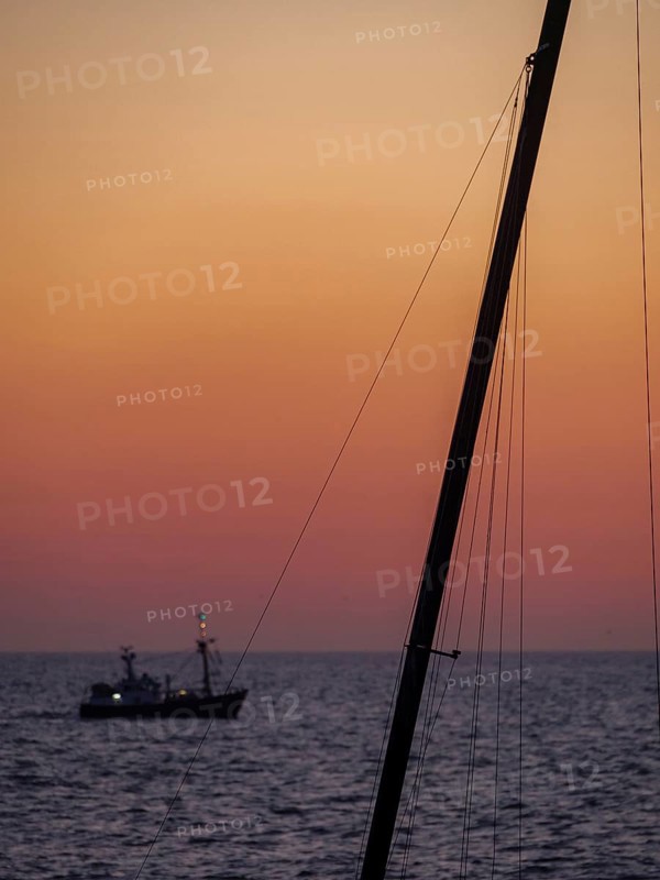 Ferrymen on the horizon, sailing mast in the foreground, atmospheric light and calm atmosphere at dusk, DE Haan, Belgium, Europe