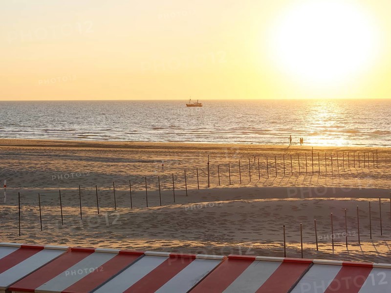 A tranquil scene on the beach with a boat on the horizon and a warm sunset, de haan, Belgium, Europe