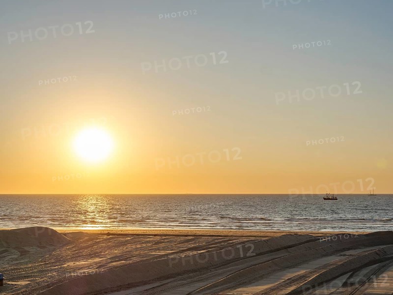 The sun sets over the sea, a boat can be seen in the distance, the atmosphere is calm and peaceful, DE Haan, Belgium, Europe
