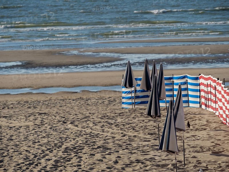 Beach view with blue-white and red-white windbreaks and calm sea in the background, de haan, Belgium, Europe