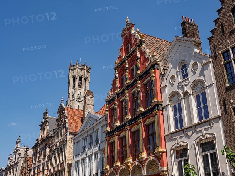 A historic street with stately brick buildings and a large tower in the background, Bruges, Belgium, Europe