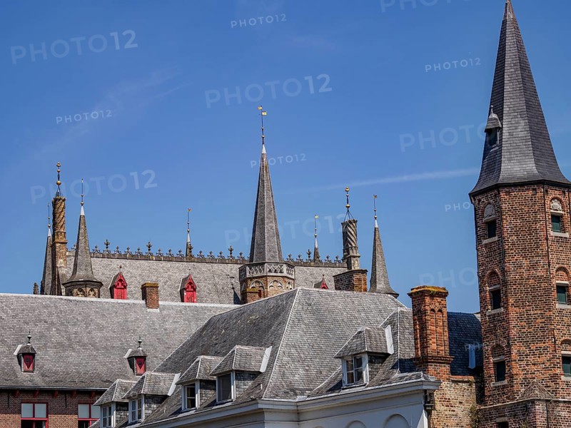Historic building with many towers and battlements, grey roofs and bricks, under a blue sky, Bruges, Belgium, Europe