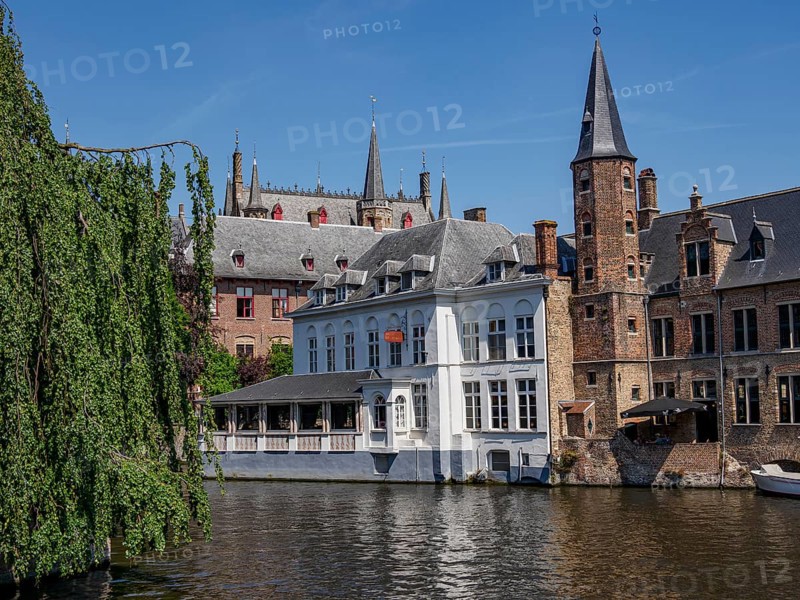 Gothic buildings and church towers reflect in the water under a clear blue sky, Bruges, Belgium, Europe