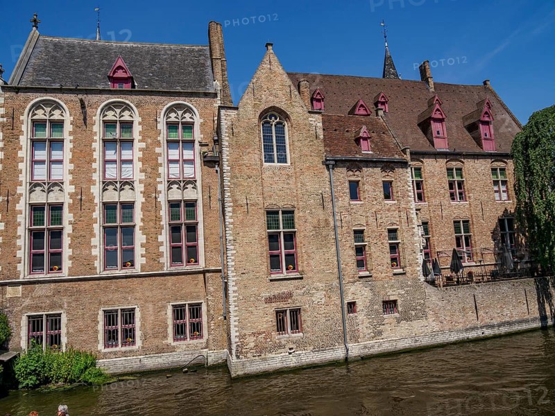 Historic buildings with brick facades along a canal under a bright blue sky, Bruges, Belgium, Europe