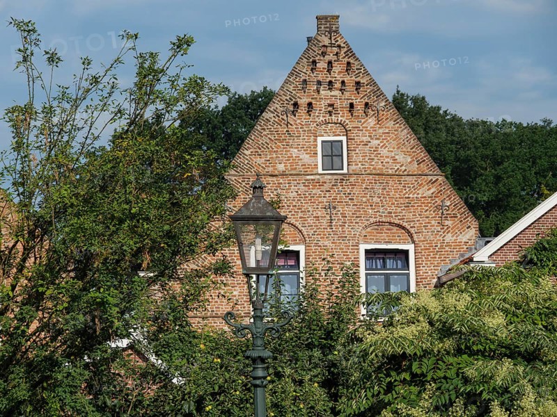 An old house with brick faÃ§ade and windows, surrounded by abundant vegetation and a classic street lamp, bredevoort, the netherlands