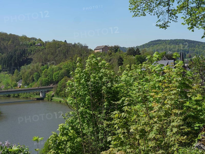 An idyllic river landscape with a bridge, surrounded by wooded hills and spring-like trees, Saarburg, Germany, Europe