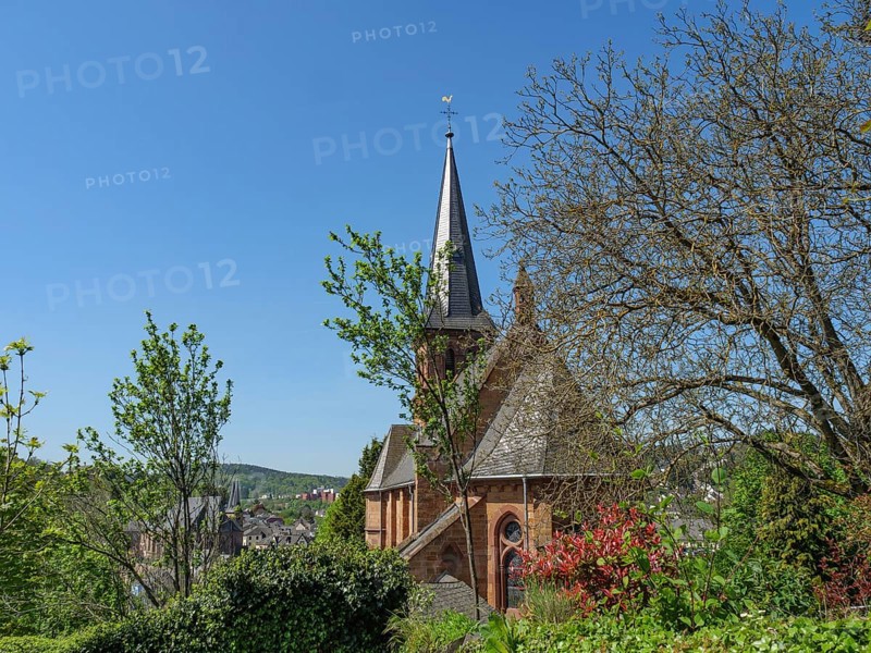A church tower rises above a tree- and plant-covered environment under a clear sky, Saarburg, Germany, Europe
