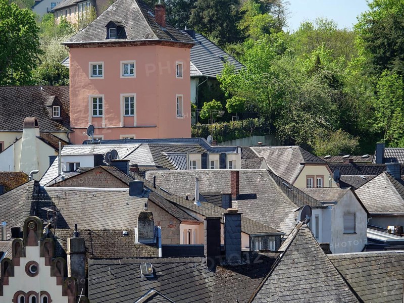 View of the roofs of a village with a pink building in the foreground and green trees in the background, Saarburg, Germany, Europe