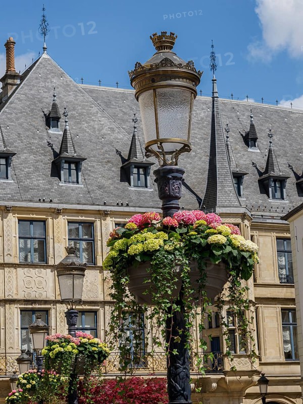 Hanging flower arrangements around an antique street lamp, behind it a historic building with several gables, gent, belgium