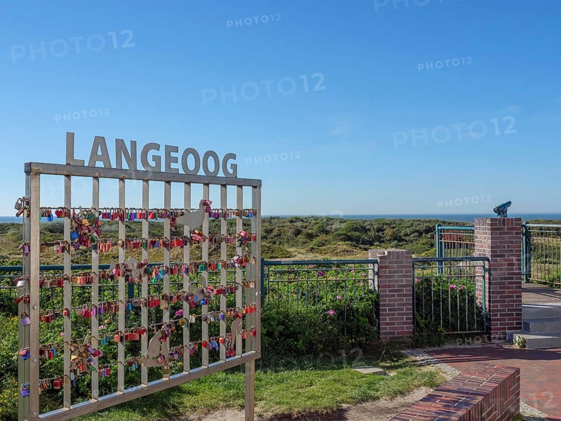 A fence with love locks in front of a vast natural backdrop under a blue sky on Langeoog, langeoog, germany