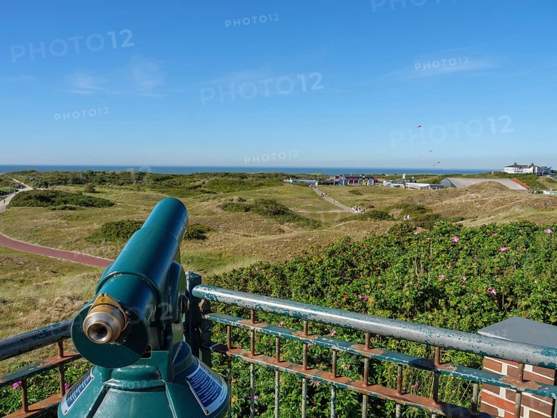 A pair of binoculars on a viewing platform with a view of the dune landscape and houses in the distance, langeoog, germany