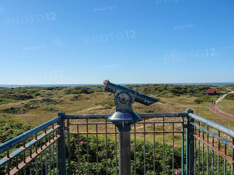 A pair of binoculars on a viewing platform with a view of a vast dune landscape and the sea, langeoog, germany