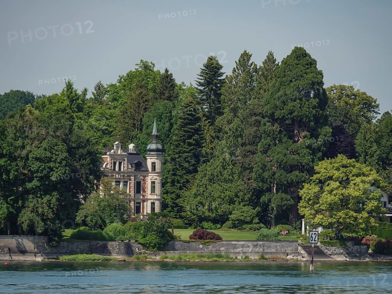 Elegant castle with characteristic towers and facades, surrounded by dense forest and water on the shore, Lindau, Lake Constance, Germany, Europe