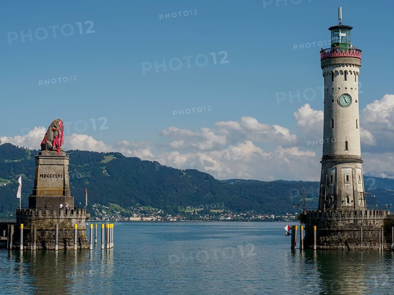 A lighthouse and a lion statue on the lakeshore with mountains in the background, Lindau, Bavaria, Germany, Europe