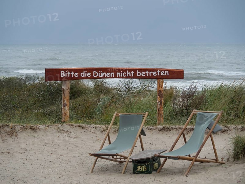 Two empty deckchairs stand on the beach in front of the sea and a warning sign prohibiting access to the dunes, juist, east friesland, germany