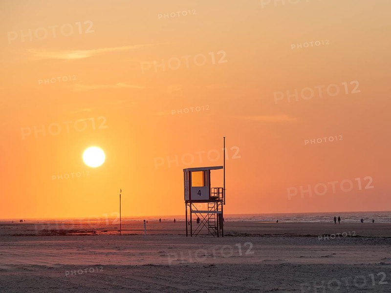 A rescue tower stands on the beach, the sky is coloured orange by a breathtaking sunset, juist, east frisia, germany