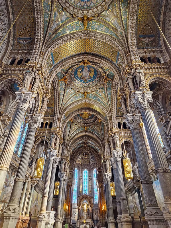Notre Dame de Fourviere in Lyon, France. Indoors view of basilica altar in Neo-Byzantine architecture style with big arches, tall columns, mosaic ceiling in blue and golden colors, stained glass art