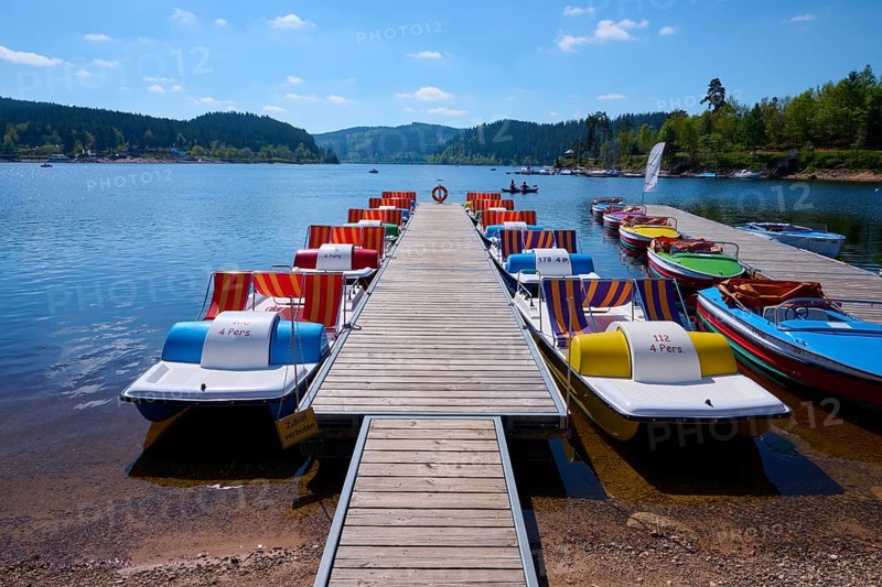 A picturesque scene with colourful pedal boats and wooden boats on a jetty in front of the Schluchsee, surrounded by mountains, spring, Schluchsee, Black Forest, Baden-Württemberg, Germany, Europe