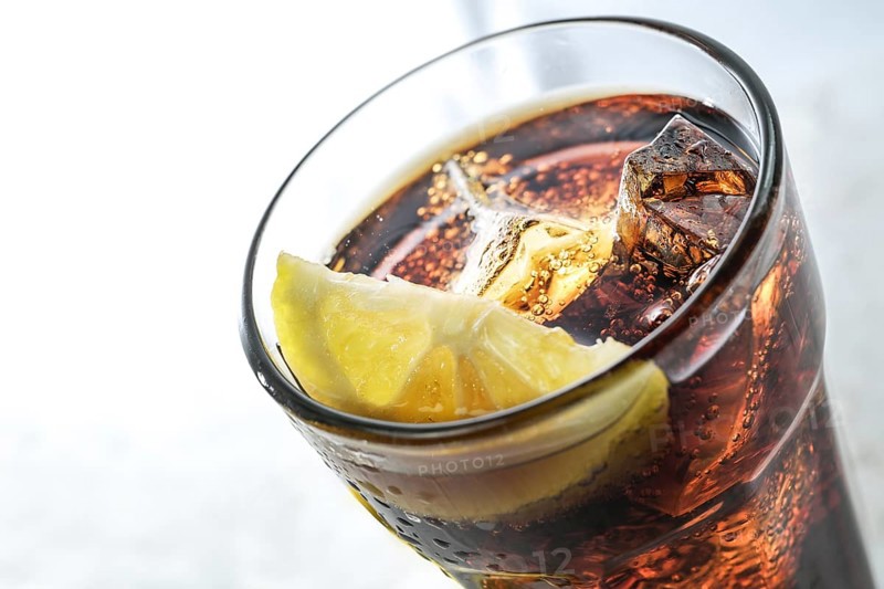 Part of a drinking glass with fresh cola, ice cubes and lemon slice, refreshing sweet caffeine drink against a light gray background, copy space, selected focus, narrow depth of field