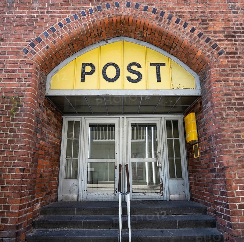 Entrance to the Post office in an historic building with a yellow sign, an old door and an arch of brick architecture in the old town of Lubeck, Germany, traditional business concept, Europe