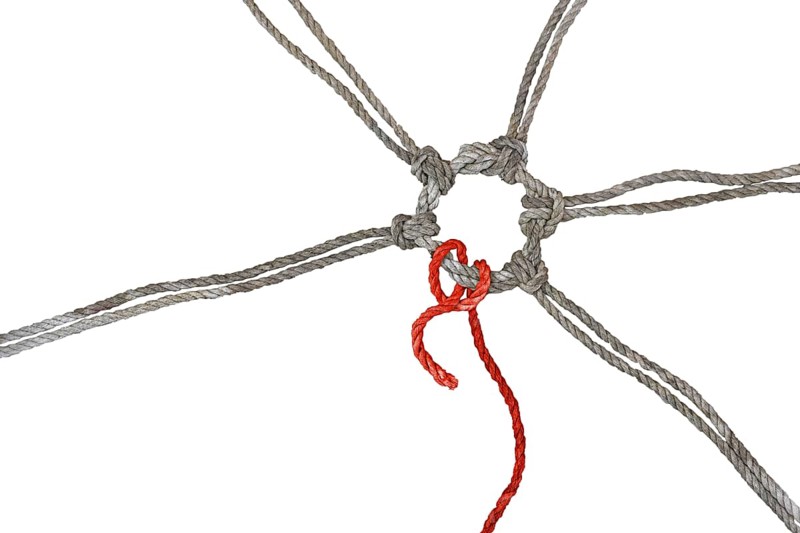 Rustic ropes join together in a knotted ring, one of them in red has a loose end, concept between cohesion, individualism and burnout, isolated on a white background, copy space