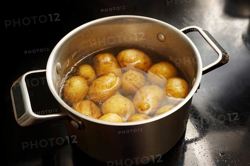 Potatoes with peel in a stainless steel pot with boiling water on the stove, healthy cooking concept, copy space, selected focus, narrow depth of field