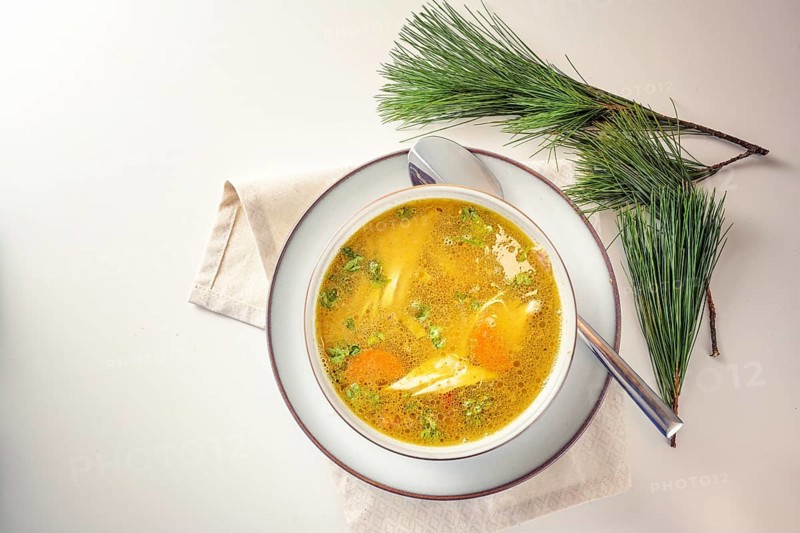 Healthy curry soup with chicken, vegetables and parsley in a bowl, home remedy against cold and flu in autumn and winter, light table with pine branches, copy space, top view from above, selected focus