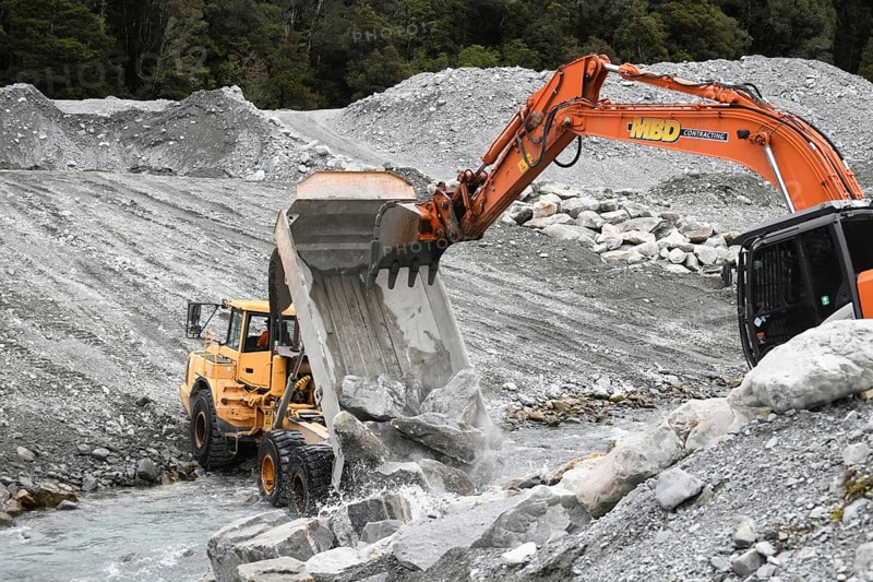OTIRA, NEW ZEALAND, SEPTEMBER 19, 2019: A tip truck dumps a load of rock to create flood water control on a West Coast river just above a railway bridge