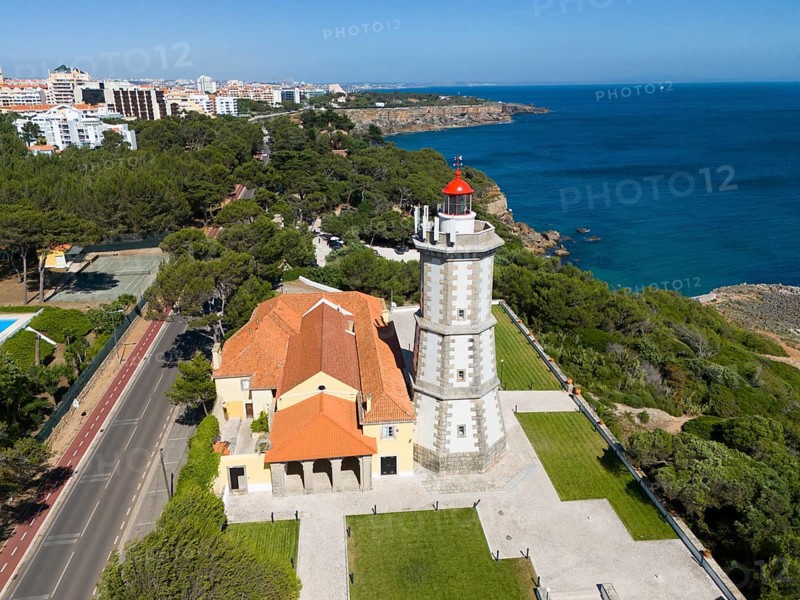 A lighthouse on the coast with a red top and a neighbouring building next to a forest and a paved road, aerial view, Farol da Guia, Cabo da Guia, Cascais, Lisbon, Lisboa, Portugal, Europe