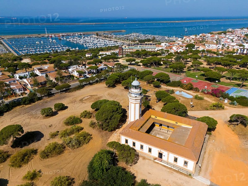 A lighthouse overlooking a coastal town and a marina, surrounded by trees under a sunny sky, aerial view, lighthouse, Mazagon, Mazagon, Cadiz province, Cadiz, Costa de la Luz, Andalucia, Spain, Europe