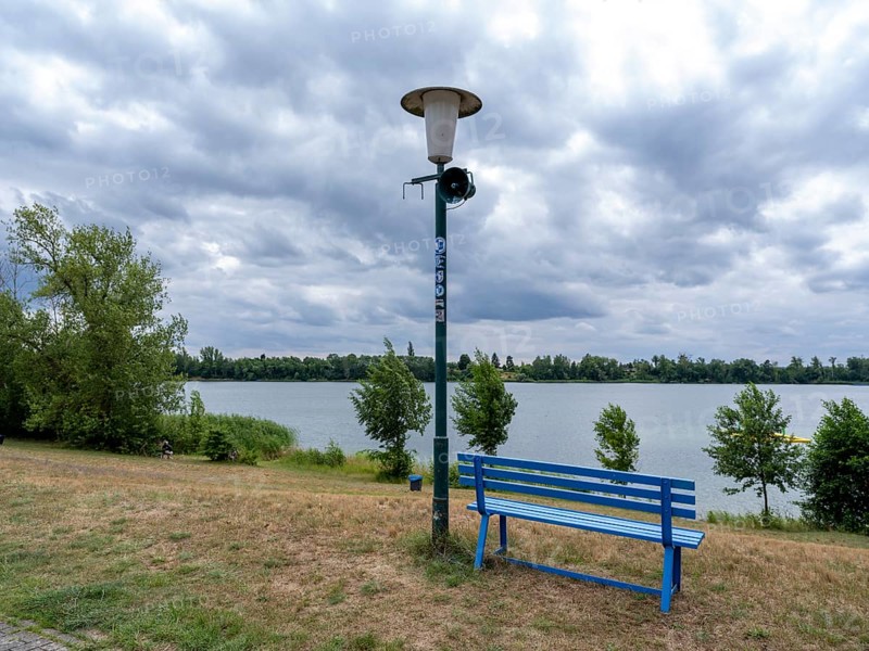 Weathered street lamp with loudspeakers next to a blue wooden bench at Lake Jersleben, Jersleben, Saxony-Anhalt, Germany, Europe