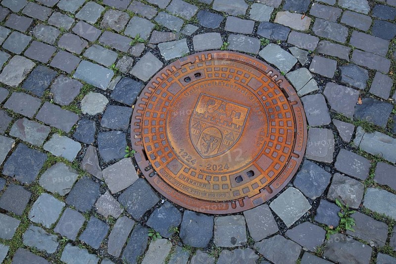 Round rusty manhole cover with city coat of arms and inscription university town, year, round, rusty, paving stones, floor, Upper Castle, Siegen, Siegerland, North Rhine-Westphalia, Germany, Europe