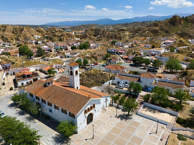 A village square with a church, houses and trees, surrounded by hills and mountains under a clear blue sky, aerial view, church, cave district, Troglodytos, Guadix, Granada, Andalusia, Spain, Europe