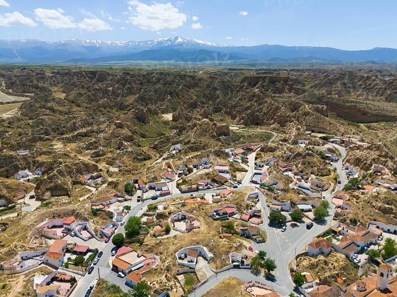 Panoramic view of a village embedded in a rocky and hilly landscape with mountains in the background, aerial view, cave dwellings, cave district, Troglodytos, Guadix, Sierra Nevada, Granada, Andalusia, Spain, Europe
